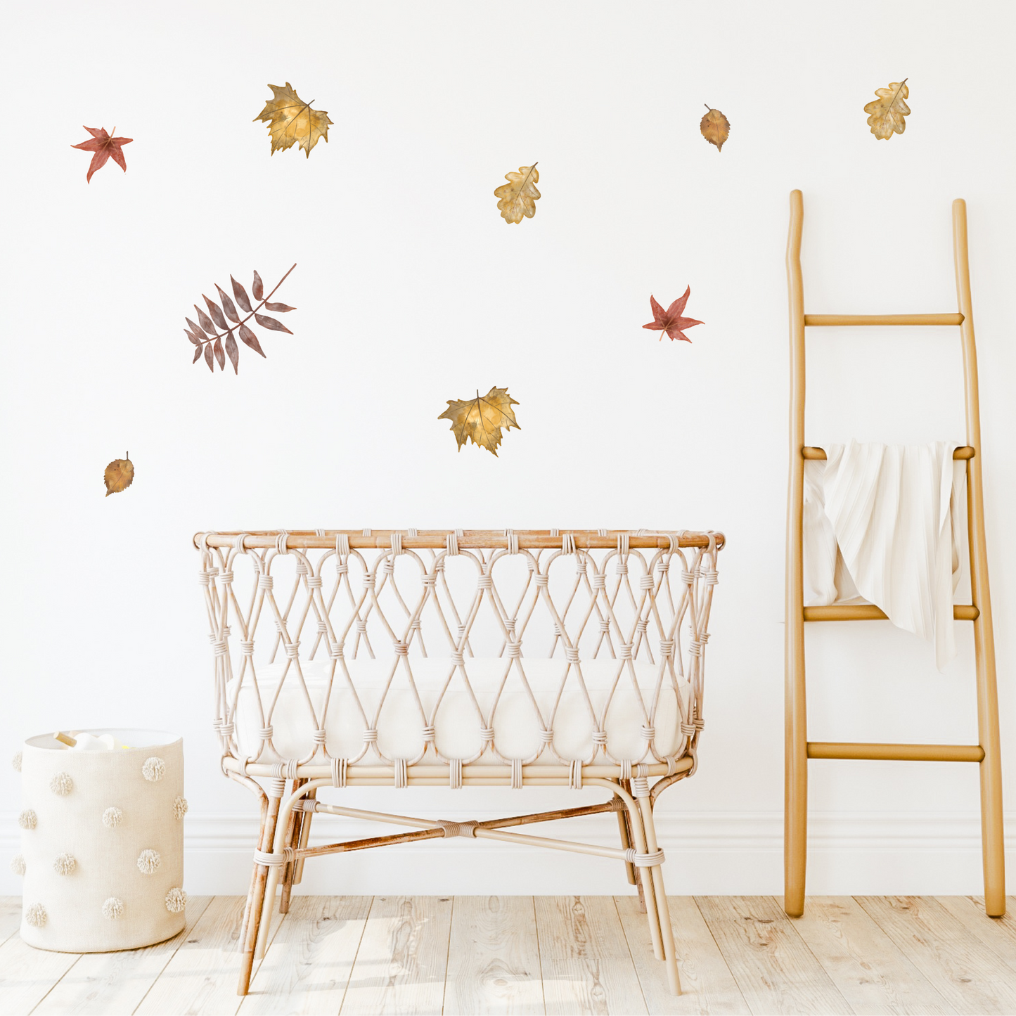 A collection of decorative wall decals of autumn leaves in warm tones, placed in a child's room on a white wall above a rattan crib. Non-toxic, eco-friendly, reusable wall stickers. Australian made.