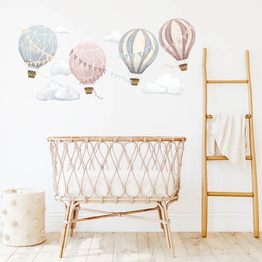 A set of colourful hot air balloon wall decals in various sizes flying across a wall, above a rattan crib and a wooden ladder in a room. Non-toxic, eco-friendly, reusable wall stickers. Australian made.