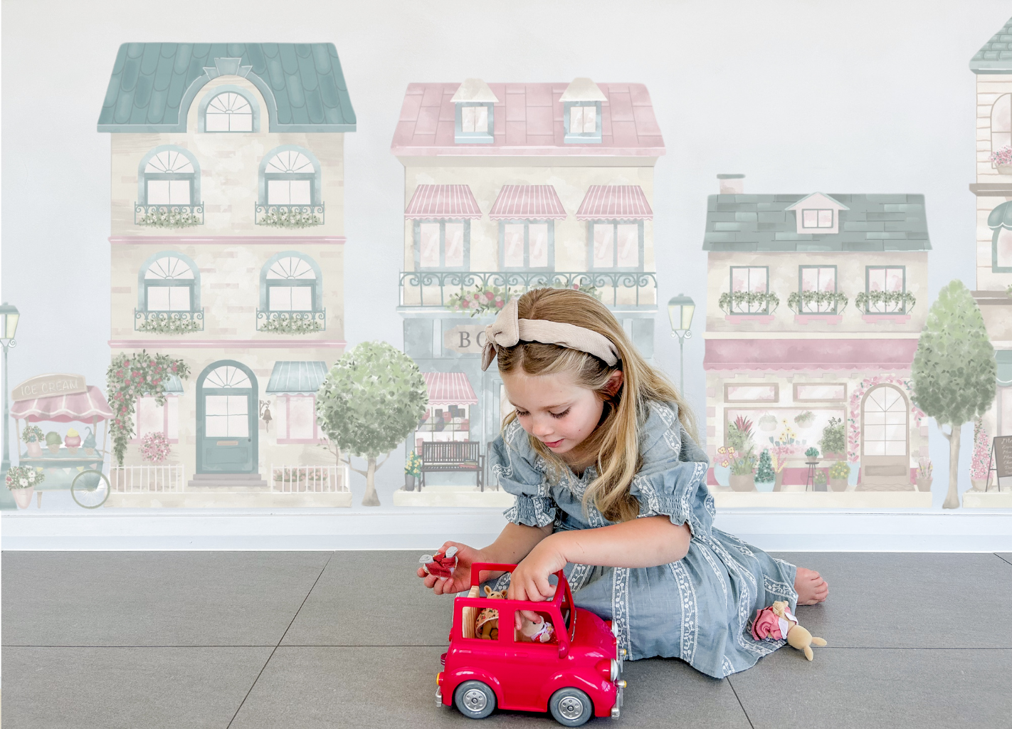 Young girl playing with a toy car in front of the Little Village wall sticker set.