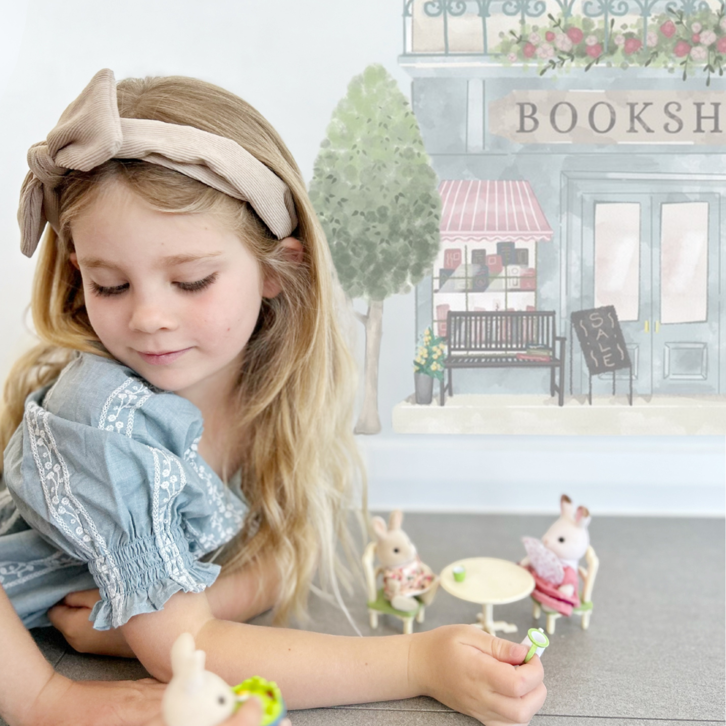 A little girl playing in front of the Little Village wall decal set.  Part of the bookshop wall sticker can be seen.  Non-toxic, eco-friendly, reusable wall stickers. Australian made.