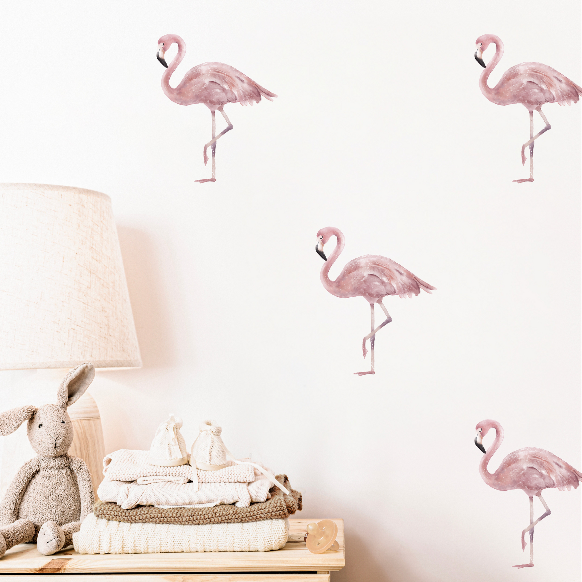 Children's bedroom wall with pink watercolour flamingo decals above a table with a lamp and plush toys. Non-toxic, eco-friendly, reusable fabric wall stickers. Australian made.