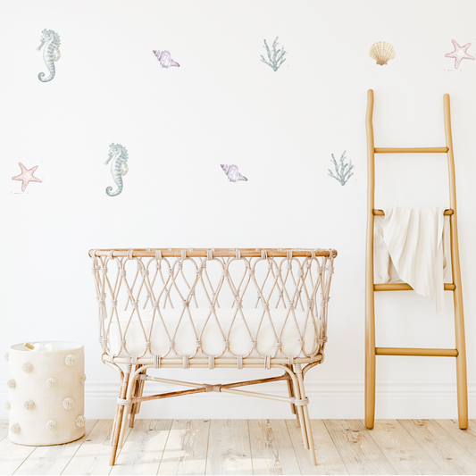 A kid's room with 'Sea Life' themed wall decals, featuring illustrations of starfish, coral, shells, and seahorses. The room includes a cane cradle, a wooden ladder, and a white wall.